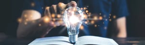 lit up lightbulb with man sitting behind and finger on the bulbfinger on the bulb